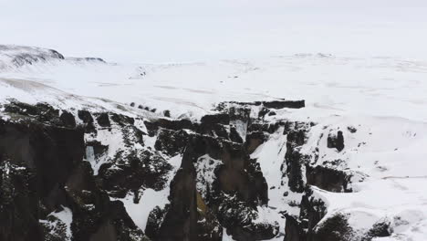 Aerial-view-backwards-over-a-snowy-gorge,-overcast-in-wintry-Iceland