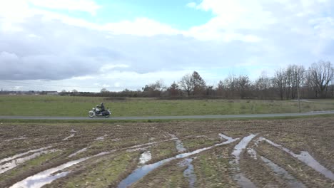 Sideways-aerial,-bike-rider-on-a-vintage-motorcycle-riding-through-countryside