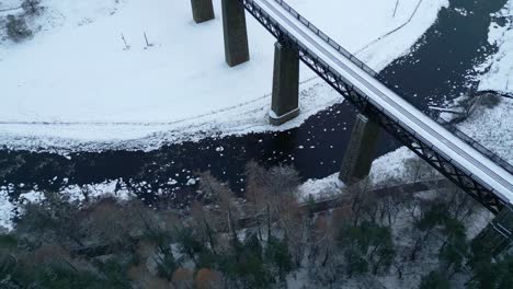 Blick-Aus-Der-Vogelperspektive-Auf-Die-Eisenbahnbrücke-über-Den-Zugefrorenen-Fluss-Und-Das-Verschneite-Tal