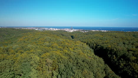 Wunderschöner-Langsamer-Flug-über-Die-Bäume-Des-Landschaftsparks-In-Gdingen---Im-Hintergrund-Das-Zentrum-Von-Gdingen---Blick-Auf-Die-Bucht-Und-Den-Charakteristischen-Wolkenkratzer-Sea-Tower