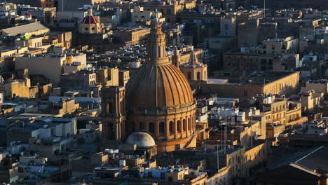Aerial-telephoto-shot-orbiting-the-Basilica-of-Our-Lady-of-Mount-Carmel,-Valletta,-sunset-in-Malta