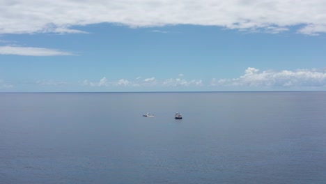 Aerial-wide-push-in-shot-of-a-small-ferry-boat-approaching-a-submarine-in-the-open-ocean-off-the-coast-of-Kailua-Kona,-Hawai'i