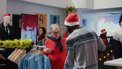 Employee-assisting-older-woman-with-picking-right-shirt-to-give-as-present-to-husband-for-upcoming-Christmas-holiday-season.-Client-browsing-through-clothes-in-xmas-adorn-fashion-shop