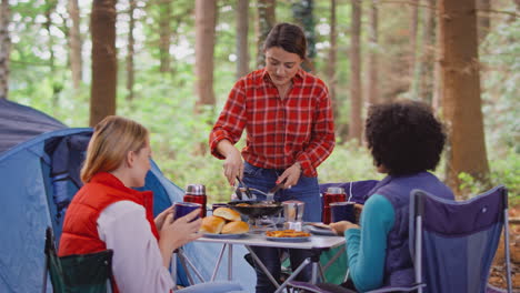Grupo-De-Amigas-De-Vacaciones-En-Camping-En-El-Bosque-Cocinando-Comida-Sentada-Junto-A-Una-Tienda-De-Campaña