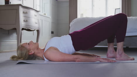 Active-Mature-Woman-Exercising-Doing-Yoga-On-Mat-At-Home