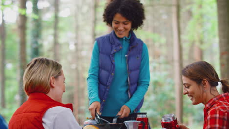 Group-Of-Female-Friends-On-Camping-Holiday-In-Forest-Cooking-Meal-Sitting-By-Tent-Together