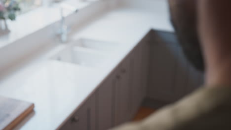 Close-Up-Of-Male-American-Soldier-In-Uniform-Looking-At-Cap-Badge-In-Kitchen-On-Home-Leave