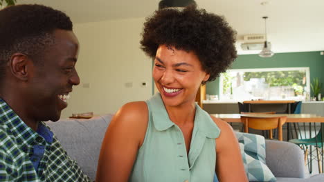 Smiling-Couple-Relaxing-On-Sofa-At-Home-Talking-And-Laughing-Together