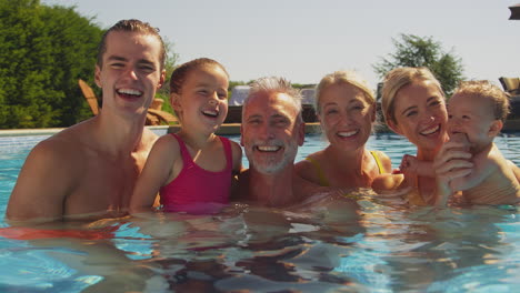 Porträt-Einer-Mehrgenerationenfamilie-Mit-Kleinem-Jungen-Im-Sommerurlaub,-Der-Sich-Im-Schwimmbad-Entspannt