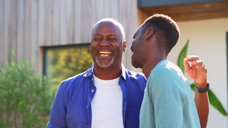 Loving-Senior-Father-With-Adult-Son-Standing-Outside-House-Laughing-Together