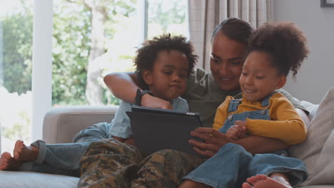 Armeemutter-In-Uniform-Zu-Hause-Auf-Urlaub-Mit-Kindern,-Die-Zu-Hause-Zusammen-Ein-Spiel-Mit-Einem-Digitalen-Tablet-Spielen