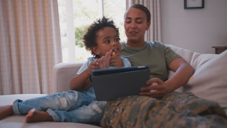 Army-Mother-In-Uniform-Home-On-Leave-With-Son-Playing-Game-With-Digital-Tablet-At-Home-Together