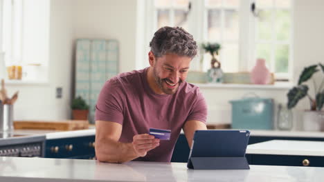 Portrait-Of-Mature-Man-With-Credit-Card-Using-Digital-Tablet-At-Home-To-Book-Holiday-Or-Shop