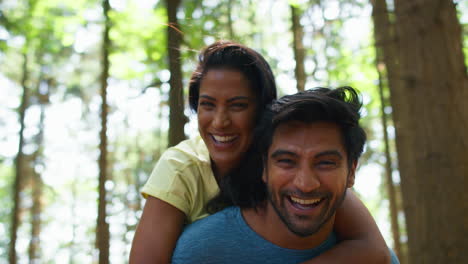 Portrait-Of-Couple-Hiking-Or-Walking-Through-Woodland-With-Man-Giving-Woman-Piggyback