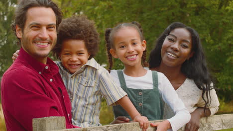 Portrait-Of-Loving-Mixed-Race-Family-Leaning-On-Fence-On-Walk-In-Countryside