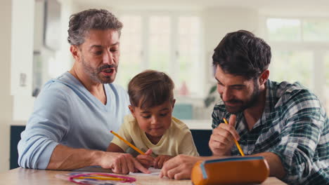 Gleichgeschlechtliche-Familie-Mit-Zwei-Vätern,-Die-Gemeinsam-Ihrem-Sohn-Am-Tisch-In-Der-Küche-Bei-Den-Hausaufgaben-Helfen