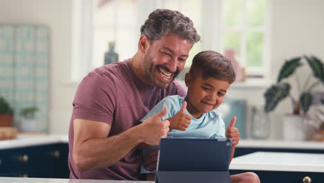 Reifer-Vater-Zu-Hause-In-Der-Küche-Mit-Sohn,-Der-Einen-Videoanruf-Auf-Einem-Digitalen-Tablet-Tätigt