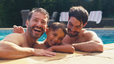 Portrait-Of-Same-Sex-Family-With-Two-Dads-And-Son-On-Holiday-In-Swimming-Pool-Together