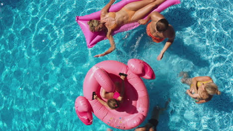 Overhead-Drone-Shot-Of-Multi-Generation-Family-With-Inflatables-On-Summer-Holiday-In-Swimming-Pool