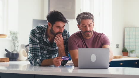 Same-Sex-Male-Couple-With-Credit-Card-Using-Laptop-At-Home-To-Book-Holiday-Or-Shop