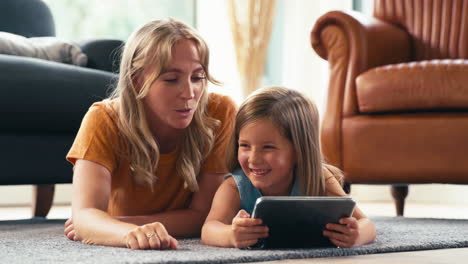 Familie-Mit-Mutter-Und-Tochter,-Die-Zu-Hause-Im-Wohnzimmer-Auf-Dem-Boden-Liegen-Und-Mit-Einem-Digitalen-Tablet-Spielen