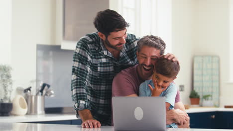 Gleichgeschlechtliche-Familie-Mit-Zwei-Vätern-Und-Sohn-Zu-Hause-In-Der-Küche,-Die-Videoanrufe-Auf-Dem-Laptop-Tätigen