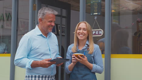 Portrait-Of-Male-And-Female-Owners-Or-Staff-Standing-Outside-Coffee-Shop-With-Digital-Tablet