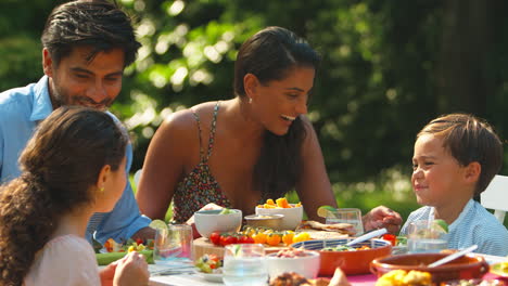 Familia-Comiendo-Comida-Al-Aire-Libre-En-El-Jardín-De-Verano-En-Casa-Juntos