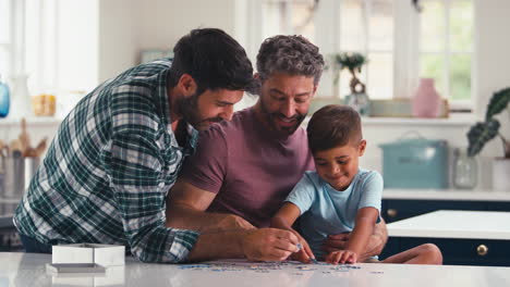 Same-Sex-Family-With-Two-Dads-And-Son-Doing-Jigsaw-Puzzle-In-Kitchen-At-Home