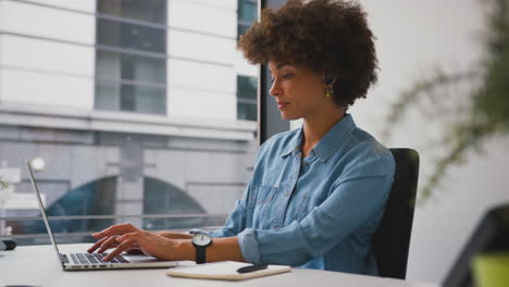 Mujer-De-Negocios-En-Una-Oficina-Moderna-Trabajando-En-Una-Computadora-Portátil-Y-Tomando-Notas-En-Un-Cuaderno