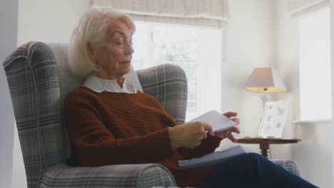 Ältere-Frau-Zu-Hause-Mit-Tragbarem-Heizkörper-Schaut-Während-Der-Lebenshaltungskosten-Energiekrise-Auf-Die-Energierechnung