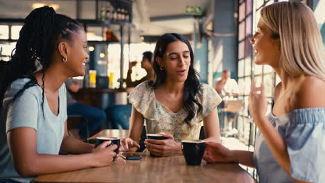 Group-Of-Female-Friends-Meeting-Up-In-Restaurant-Or-Coffee-Shop-Looking-At-Mobile-Phone