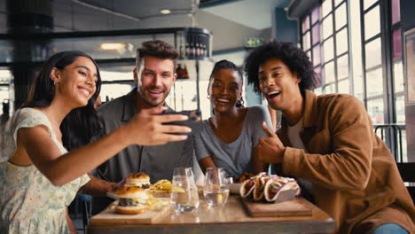 Grupo-De-Amigos-Reunidos-En-Un-Restaurante-Posando-Para-Un-Selfie-En-Un-Teléfono-Móvil-Con-Comida