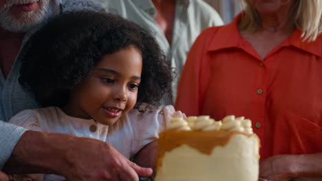 Granddaughter-Cutting-Slice-From-Cake-Celebrating-Birthday-With-Multi-Generation-Family-At-Home