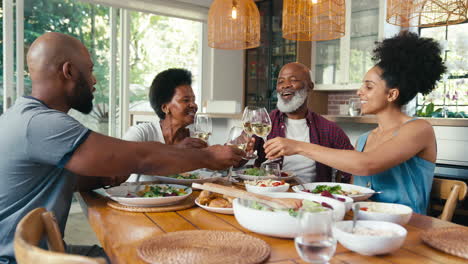 Ältere-Eltern-Mit-Erwachsenen-Nachkommen-Sitzen-Am-Tisch-Und-Jubeln-Vor-Dem-Essen-Zu-Hause-Mit-Wein
