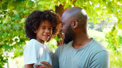 Loving-Father-Holding-Son-In-Arms-In-Summer-Garden-With-Trees