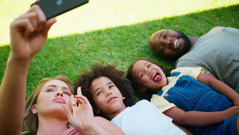 Overhead-Shot-Of-Multi-Racial-Family-Lying-On-Grass-Taking-Selfie-On-Mobile-Phone