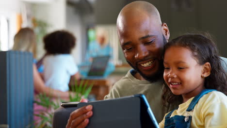 Padre-E-Hija-Usando-Una-Tableta-Digital-En-Casa-Con-Una-Familia-Multigeneracional-En-Segundo-Plano