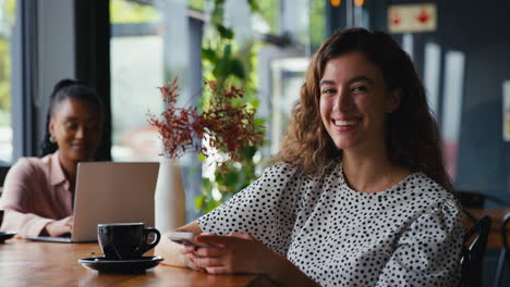 Portrait-Of-Smiling-Young-Businesswoman-Sitting-In-Coffee-Shop-Using-Mobile-Phone