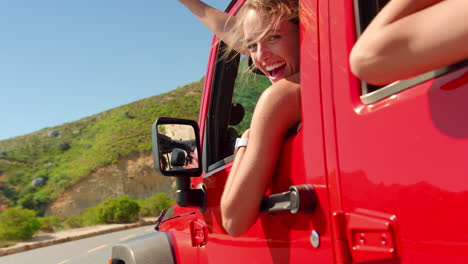 Group-Of-Laughing-Female-Friends-Waving-Through-Side-Windows-Of-Open-Top-Car-On-Road-Trip