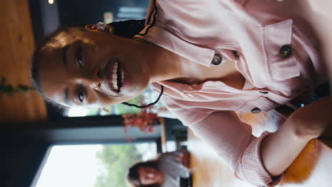 Vertical-Video-Of-Businesswoman-Wearing-Wireless-Headphones-Making-Call-On-Mobile-Phone-In-Cafe