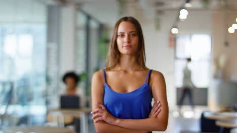 Portrait-Of-Serious-Young-Businesswoman-Standing-In-Busy-Modern-Open-Plan-Office