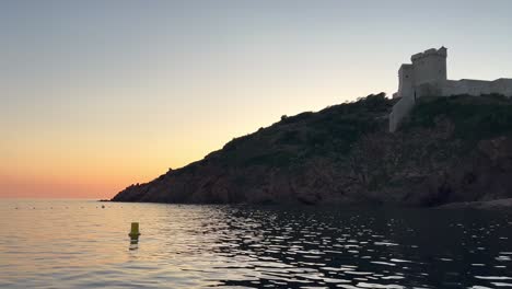 Girolata-castle-at-sunset-seen-from-sailing-boat-touring-Corsica-island-in-France