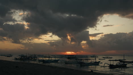 Barco-En-La-Playa-Del-Mar-Con-La-Luz-Del-Sol-Del-Amanecer-A-Través-Del-Cielo-Dorado-De-Nubes-En-El-Puerto-De-Bali