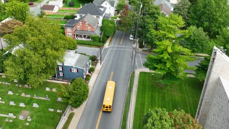 Yellow-school-bus-driving-into-American-town-to-drop-off-elementary,-middle,-and-high-school-students-in-USA