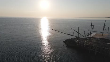 Aerial-seascape-view-over-a-trabucco,-a-traditional-fishing-machine,-on-the-italian-coastline,-at-sunset