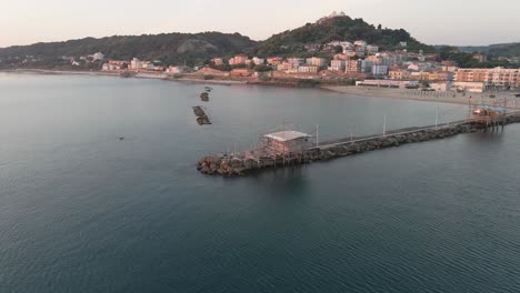 Aerial-landscape-view-of-a-trabucco,-traditional-fishing-machine,-on-the-italian-seashore,-at-sunset