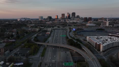Filmische-Luftaufnahme-Des-Downtown-Atlanta-Freeway-Mit-Blick-Auf-Berühmte-Skyline-Gebäude-Im-Hintergrund-Bei-Sonnenuntergang,-Verkehr-Auf-Der-Autobahn-In-Einer-Modernen-Stadt-In-Den-USA