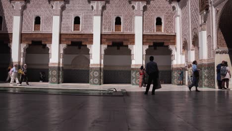 Exploring-the-sunny-interior-of-Ben-Youssef-Islamic-College,-a-masterpiece-of-craft-and-architecture,-in-vibrant-Marrakesh,-with-tourist-strolling-around