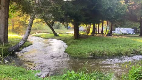 Flowing-water-on-the-zigzag-river-at-the-campsite-in-the-woods,-handheld
